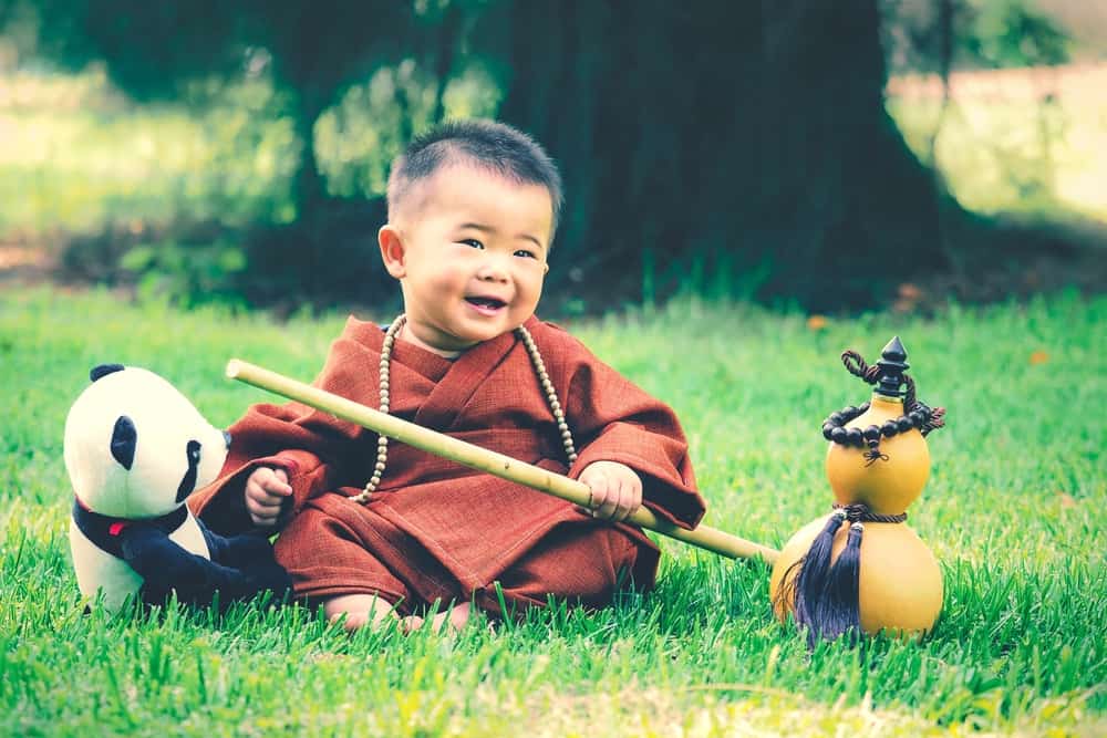 100 Best Kids Birthday Party Ideas 21 Little boy in a monk costume posing beside a panda bear.