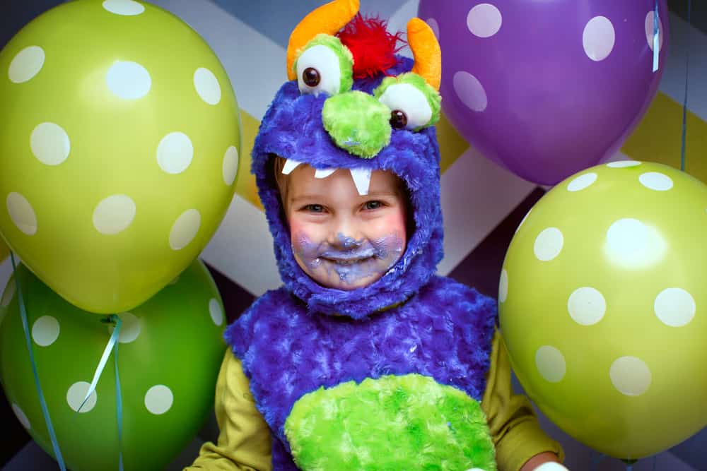100 Best Kids Birthday Party Ideas 15 Little boy in a monster costume surrounded by colorful dotted balloons.