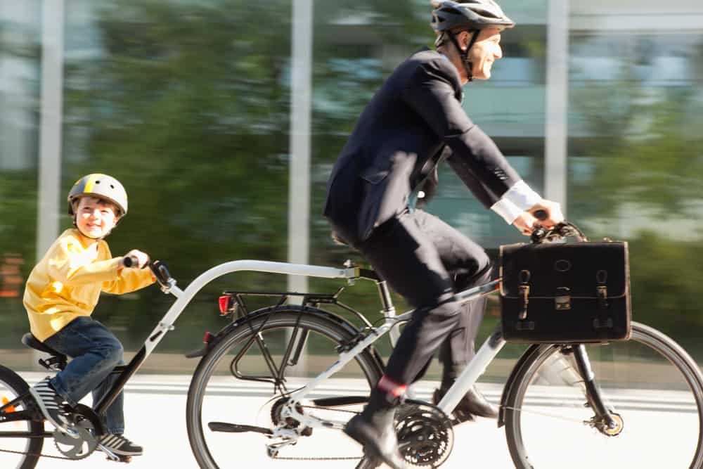 Father and son on a bicycle trailer riding  down the street.