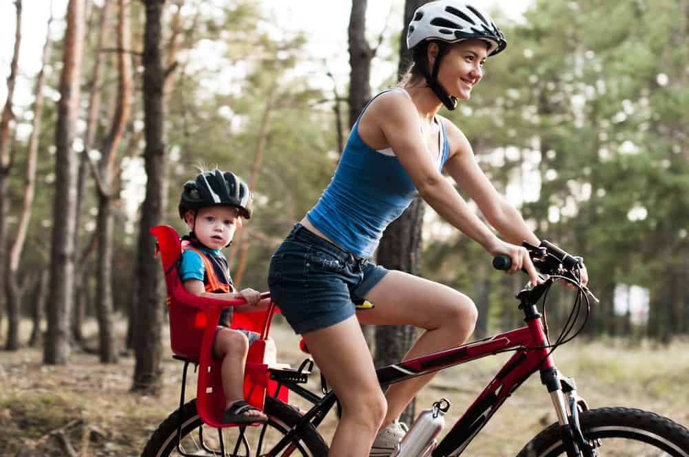 Mother riding a bike with her kid on a child seat.