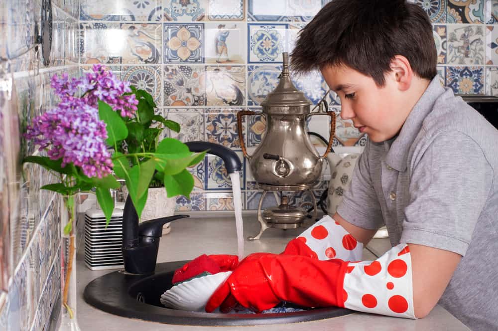 9 Best Chores for 10-12 Year Olds 9 Boy with red gloves washing dishes in the kitchen.