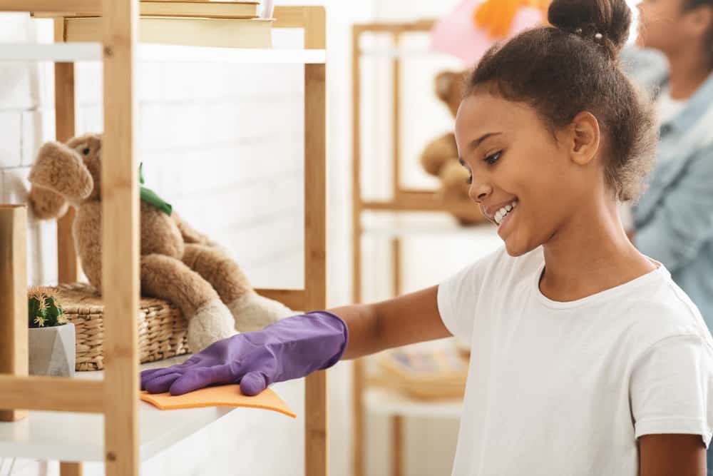 Chores for 10-12 year olds: Girl dusting shelves at home.