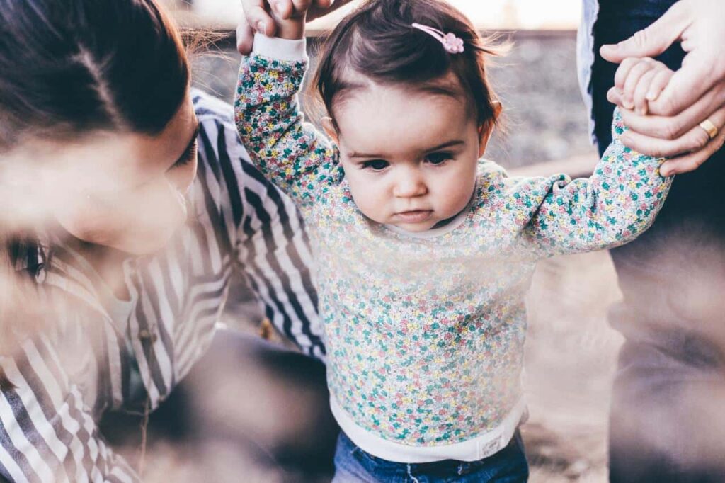 Parents guiding their little girl while walking.