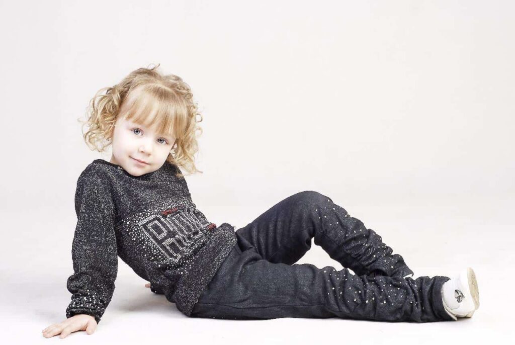 Girl in sweatshirt and pants posing on the floor.