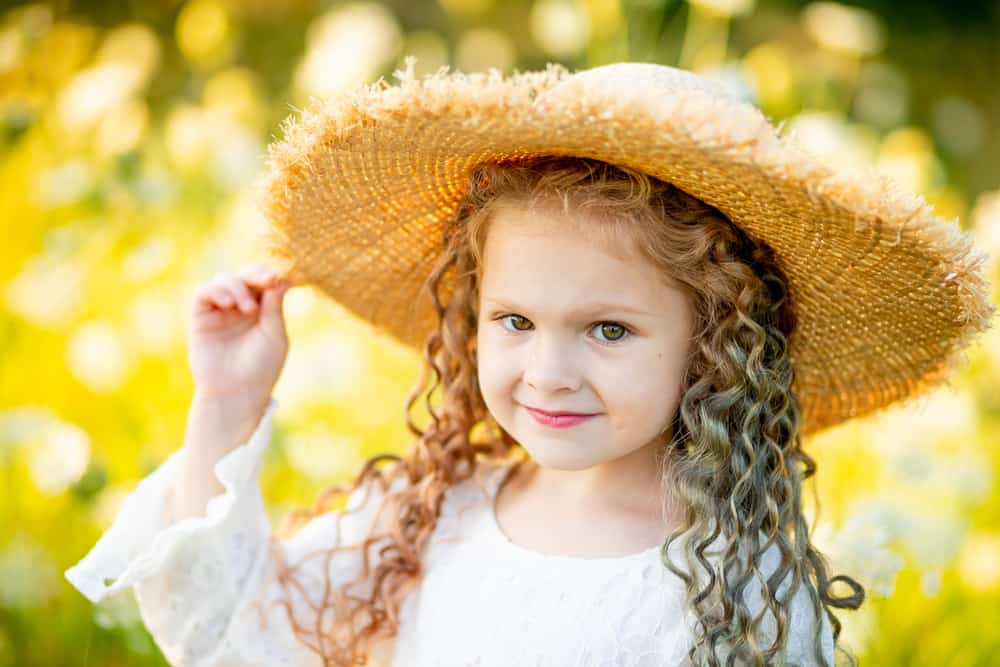 Little girl wearing straw hat posing against the summer field.