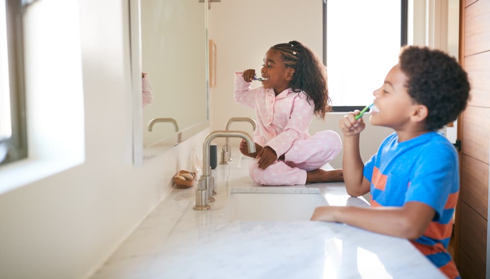 20 Best Chores for 7-9 Year Olds 3 Kids facing the vanity sink while brushing their teeth.