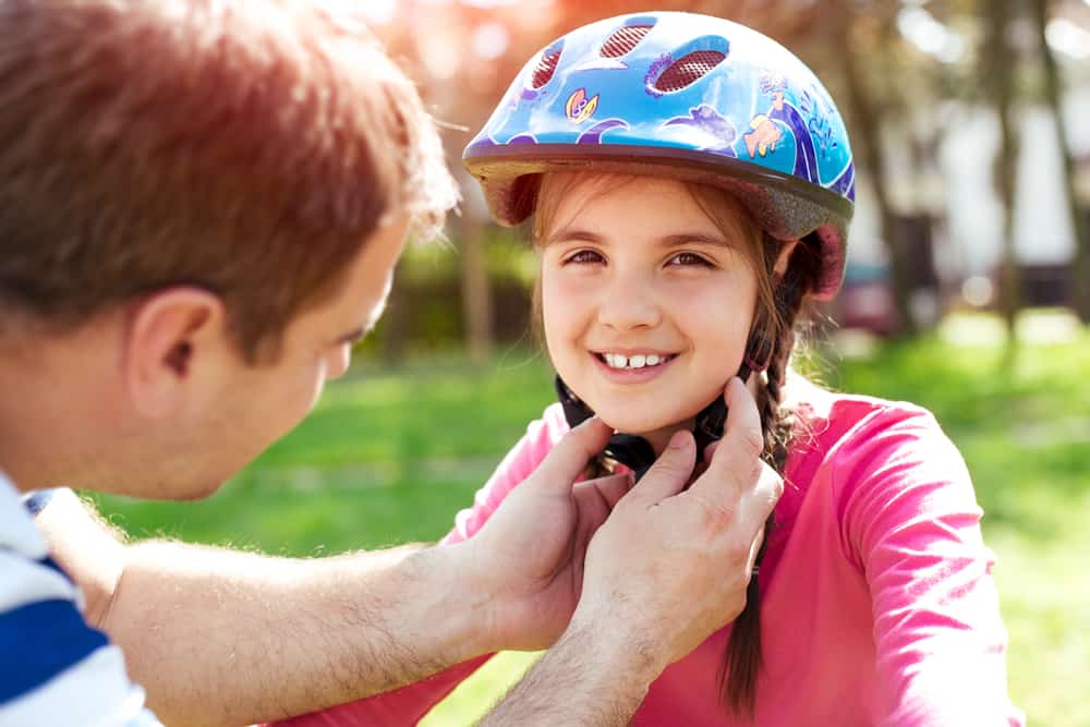 Father putting safety helmet on her daughter.