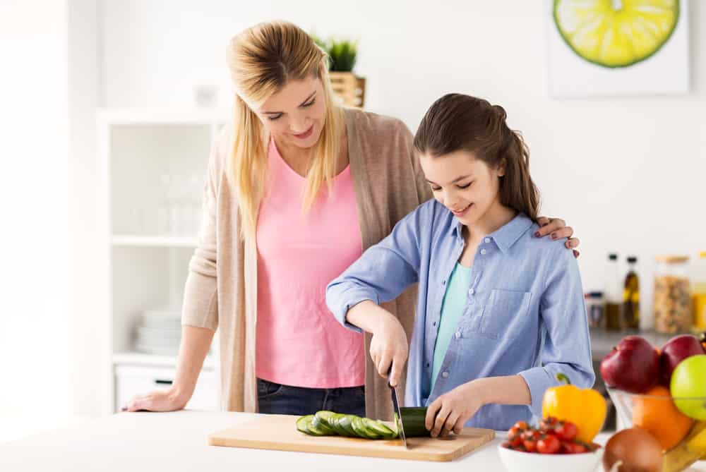 44 Best Chores for Teenagers 19 Mother guiding her daughter in cooking meal.