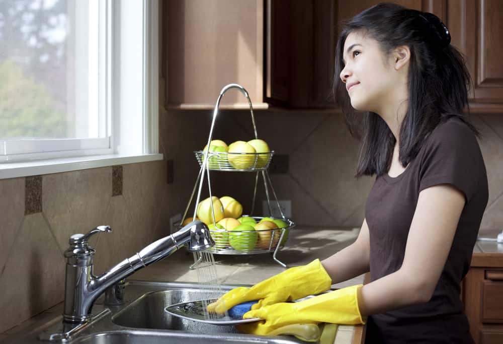 44 Best Chores for Teenagers 9 Teen washing dishes in the kitchen while looking out the window.