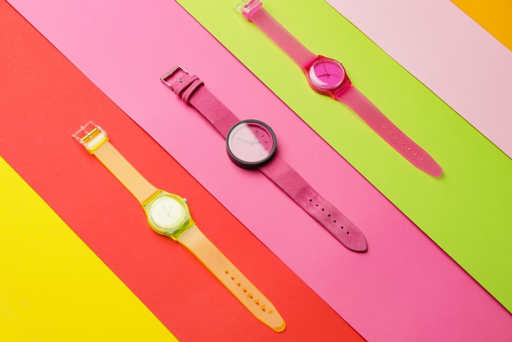 Pink and yellow analog watches for kids against multicolored background.