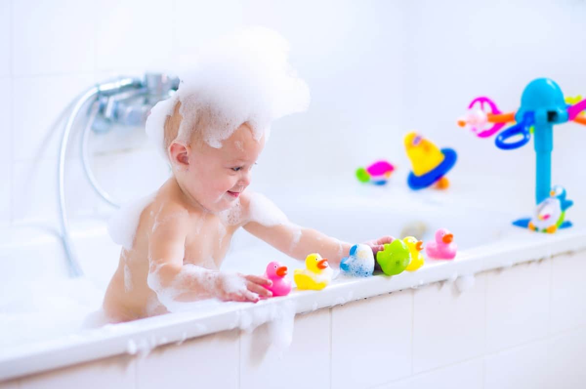 Baby in bathtub playing with floating toys.