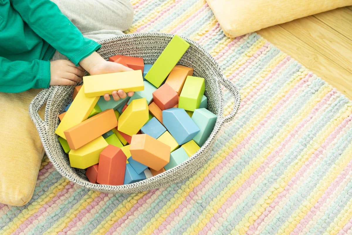 20 Best Chores for 3-4 Year Olds 3 Kid pick up toys and put it in a bin against the striped carpet.