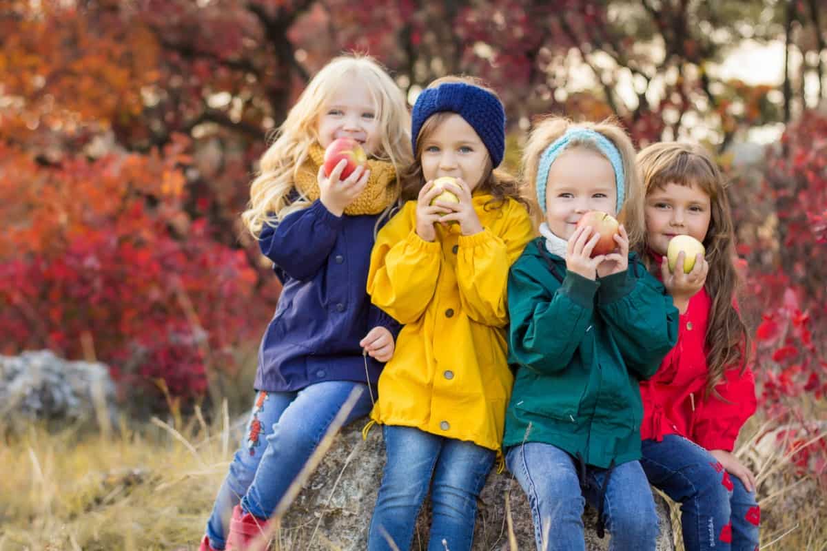 Little girls in colorful jackets holding fruits.
