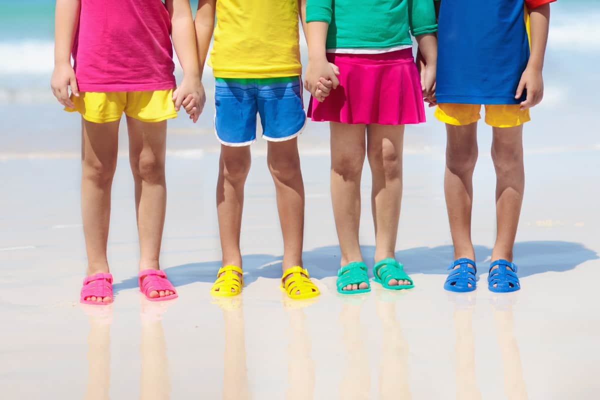 Kids wearing colorful sandals on the beach.
