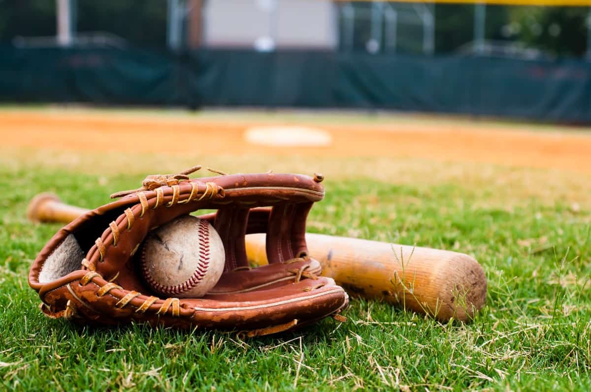 Baseball glove, ball, and bat on a field.