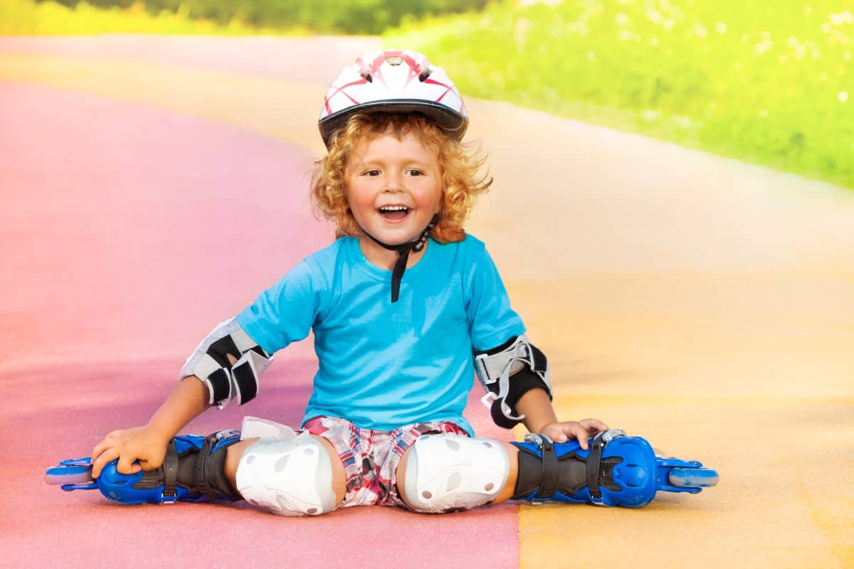 Little boy wearing rollerblades resting on the track field.