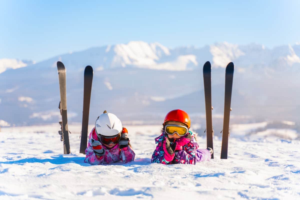 12 Popular Types of Skis for Kids 2 Kids lying on snow with skis nearby.