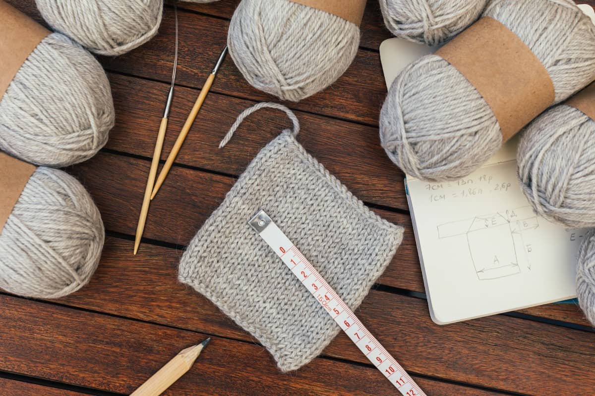 Gray knitting yarns, needles, and pencil against wooden background.