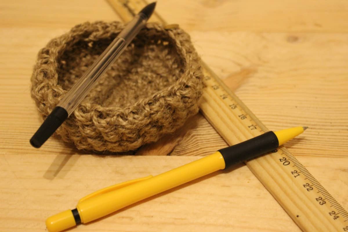 Pens, knitted holder, and ruler on the wooden table.