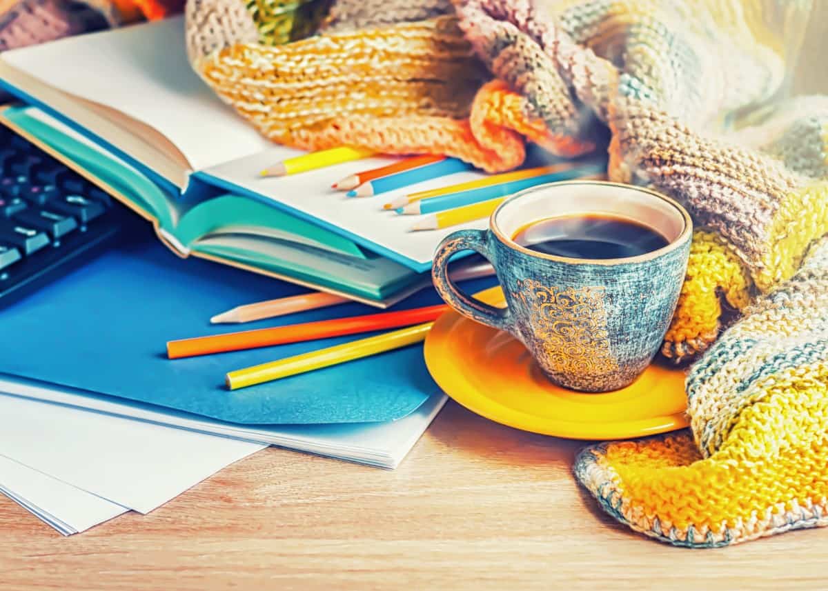 Multicolored pencils, knitted blanket, and a cup of coffee on a wooden table.