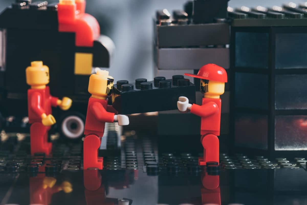 Lego figurines carrying a black Lego brick.