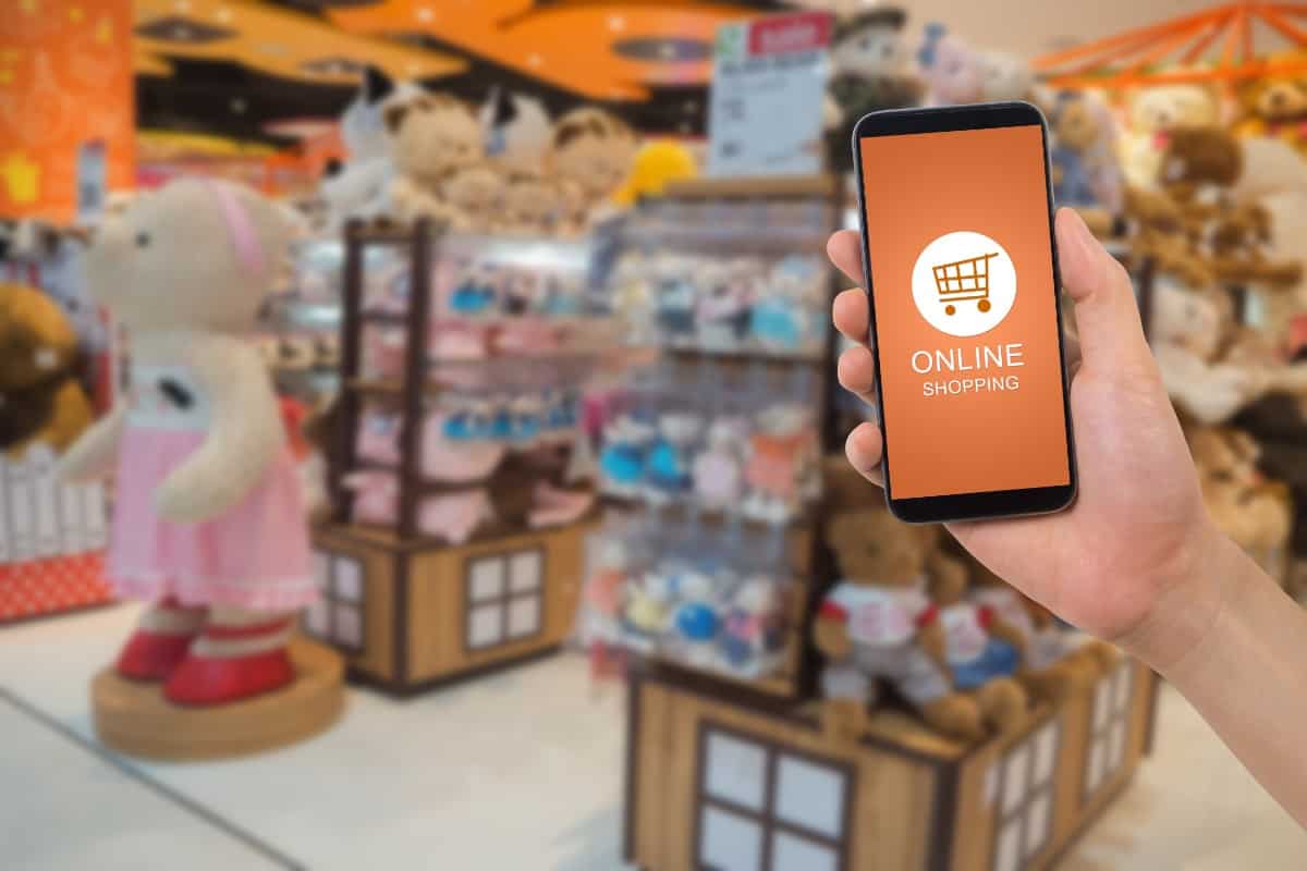 Hand holding a phone with online shopping display against the toy store.