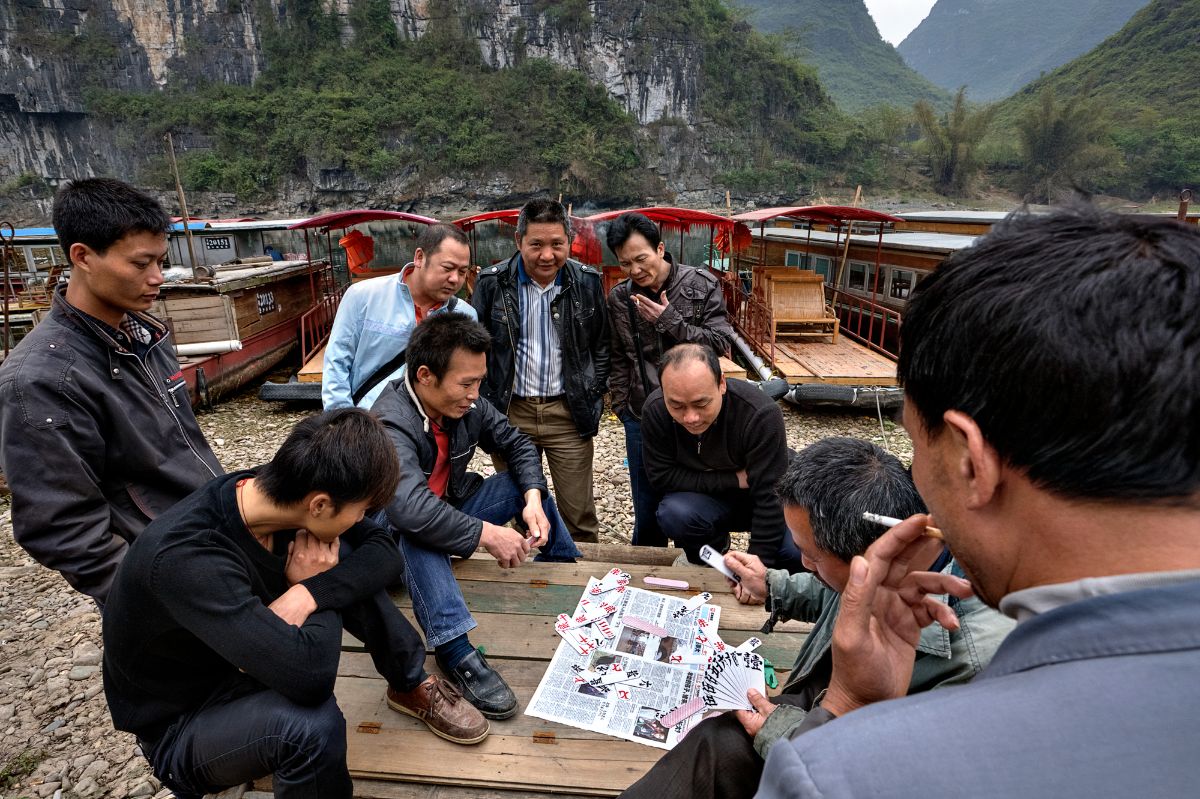 Group of Chinese people playing cards near a dock.