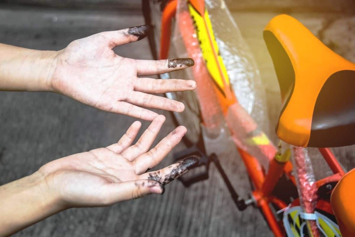 Mountain Bike Chain: How Often Should You Oil? 4 Hands stained with oil beside a bike on rest.