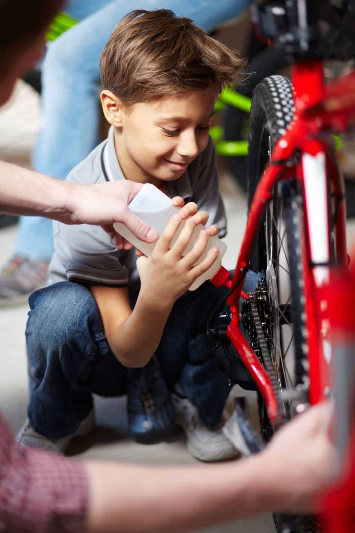 Mountain Bike Chain: How Often Should You Oil? 5 Young boil applying oil on a red bike with the help of an adult.