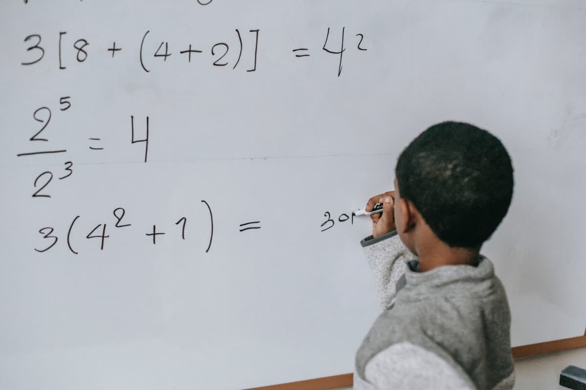 Little boy solving math equation on the white board.