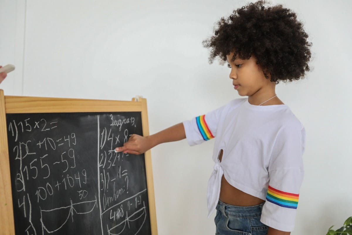 Little girl solving math equation on the chalk board.